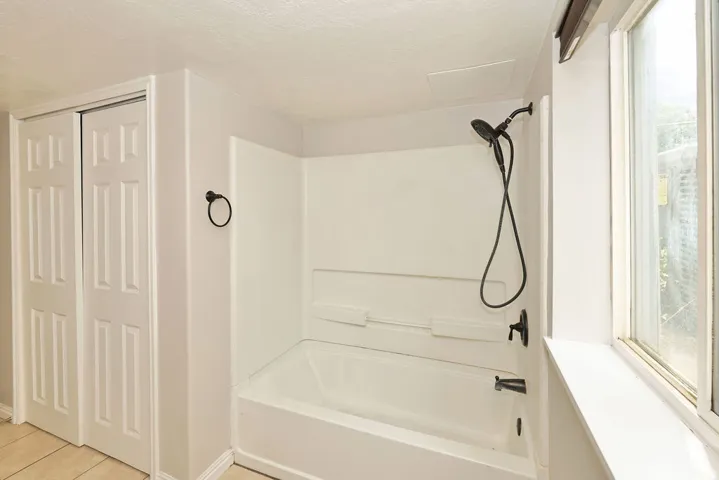 Bathtub and shower combination featuring a matte black showerhead and faucet, white surround, and a large window