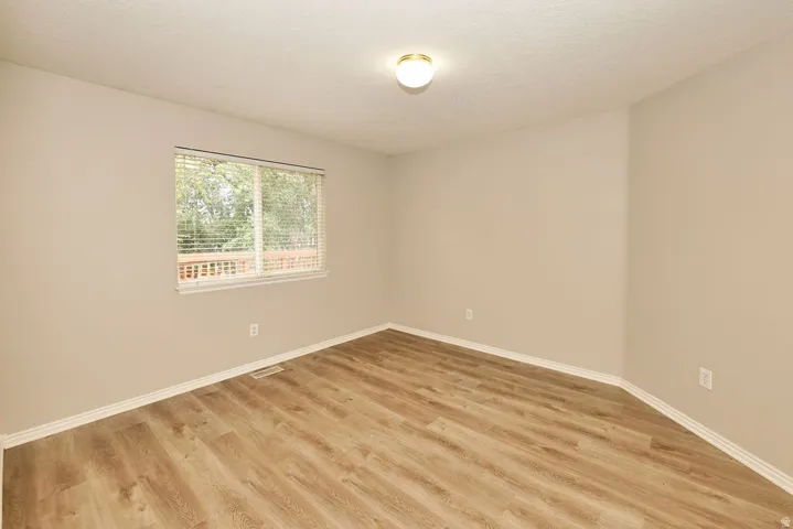 Room featuring wood-finish flooring, neutral wall tones, white trim, and a window with horizontal blinds