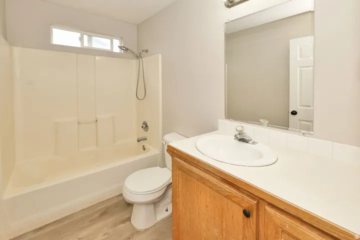 Bathroom featuring a combination bathtub and shower with a window, single vanity with a laminate countertop, wood-finish cabinetry, and a mirrored medicine cabinet
