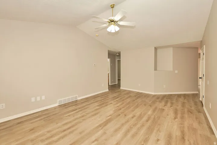 Spacious living area featuring wood-finish flooring, vaulted ceilings, a ceiling fan, and neutral wall tones
