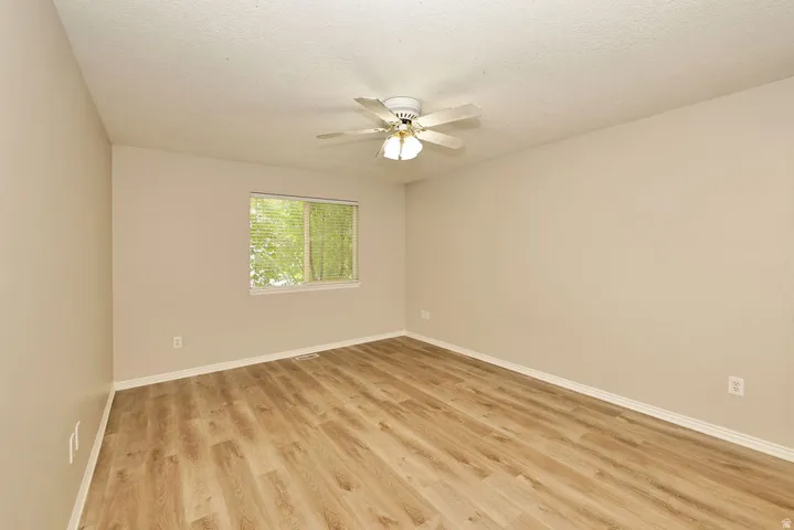 Neutral-toned room featuring wood-finish flooring, a ceiling fan with integrated lighting, and a window with blinds