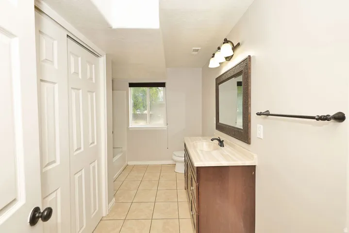 Bathroom featuring a dark wood-finish vanity with a single basin, framed mirror, and three-light sconce