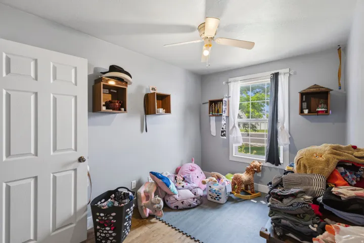 Room featuring a window with natural light, a ceiling fan with integrated lighting, wood-finish flooring, and built-in wall-mounted shelving