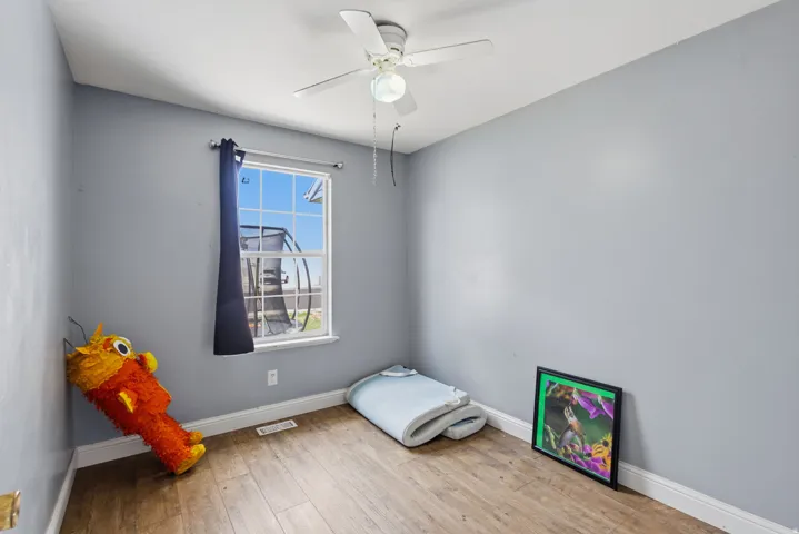 Room featuring wood-finish flooring, a ceiling fan, and a window providing natural illumination
