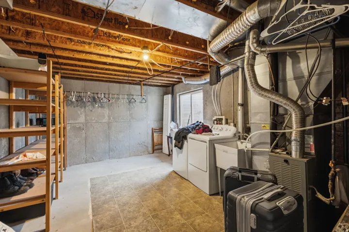 Utility room featuring exposed ceiling joists, concrete walls, a laundry sink, and a washer and dryer