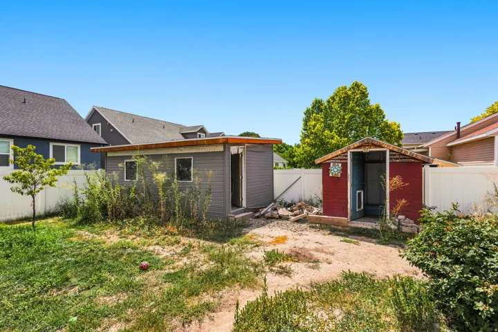 Backyard area featuring two storage sheds, a white privacy fence, and a young deciduous tree