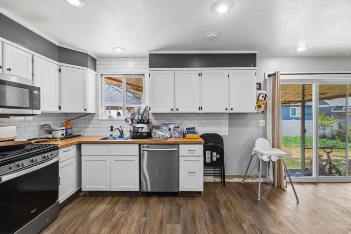 Kitchen featuring white shaker-style cabinetry, wood-finish countertops, subway tile backsplash, stainless steel appliances, and wood-finish flooring