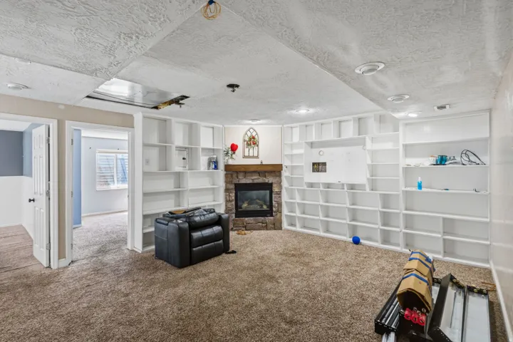 Spacious room featuring extensive built-in shelving, a stone-faced fireplace with a wood mantel, and recessed ceiling lighting