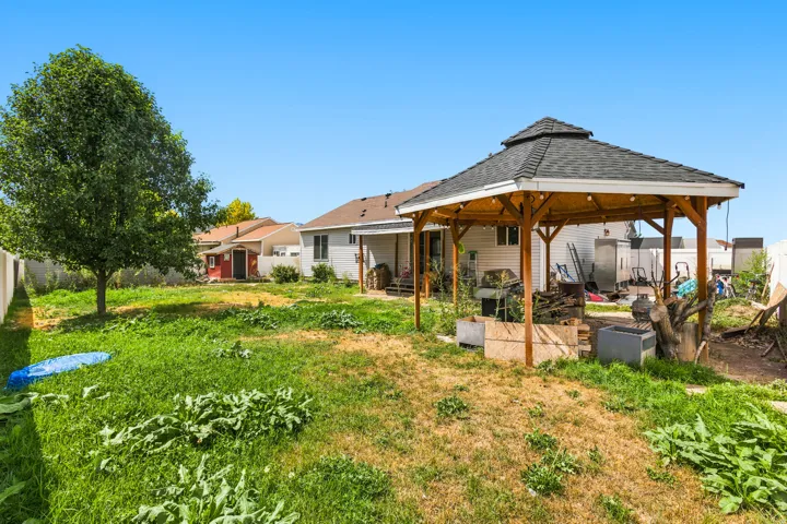Expansive yard featuring a wooden gazebo with a shingle roof, a mature tree, and a partial privacy fence