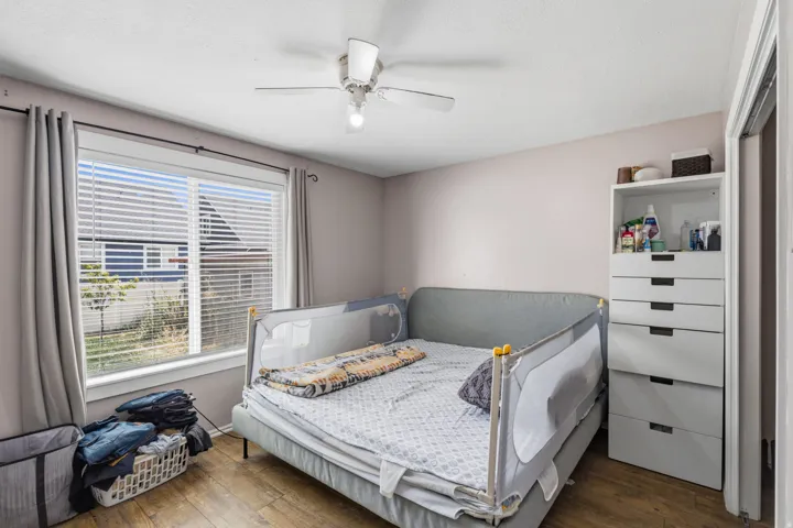 Room featuring wood-finish flooring, a ceiling fan with integrated lighting, and a window with blinds and drapes
