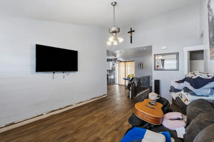 Living area featuring wood-finish flooring, white shiplap-style wall, and a ceiling fan with integrated lighting