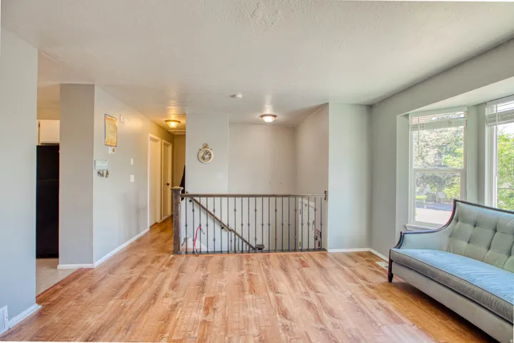 Expansive room featuring wood-finish flooring, a decorative metal railing, and a bay window