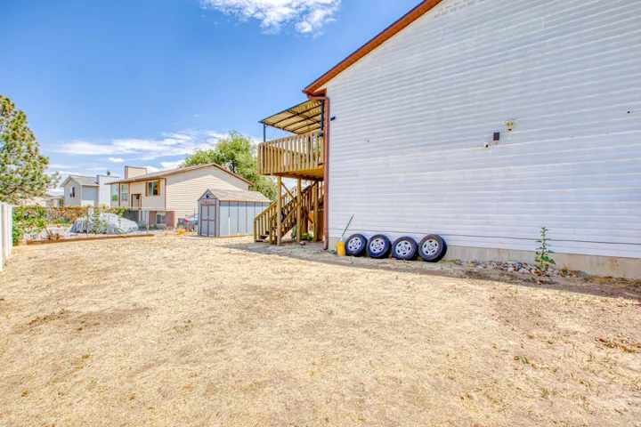 Expansive backyard featuring a wood deck with stairs, a shed, and white vinyl siding on the property