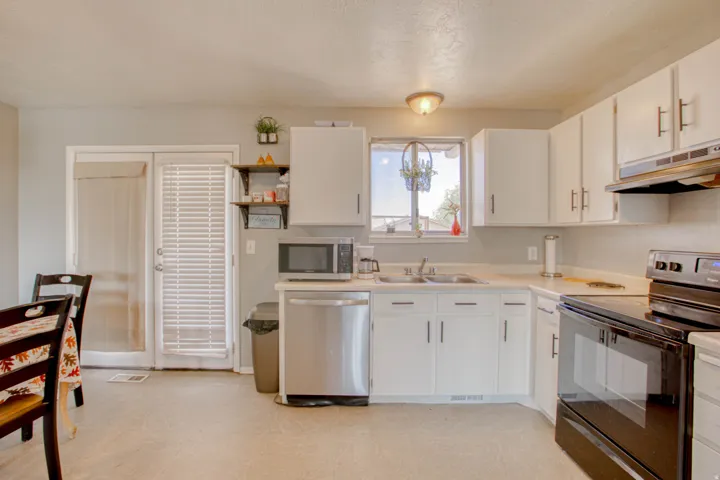 Kitchen featuring white cabinetry with brushed nickel hardware, a stainless steel dishwasher, a double basin sink beneath a window, and a range with an overhead microwave