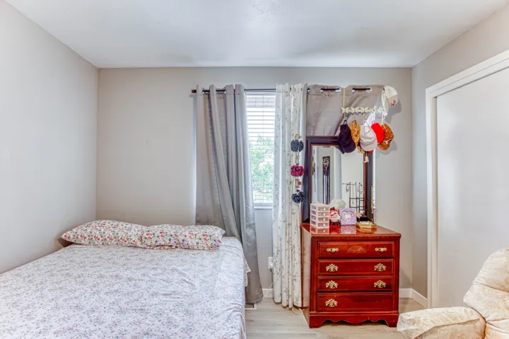 Bright room featuring light-colored walls, wood-finish flooring, and a window with blinds and curtains