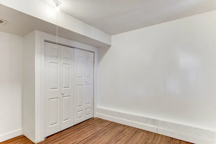 Room featuring wood-finish flooring, white painted walls, and a white bi-fold closet