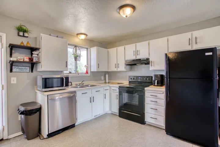 Kitchen featuring white cabinetry, light-toned countertops, a stainless steel dishwasher, a black range with an overhead vent, and a black refrigerator