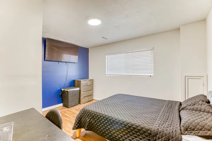 Bedroom featuring wood-finish flooring, a wall-mounted television, and a window with blinds