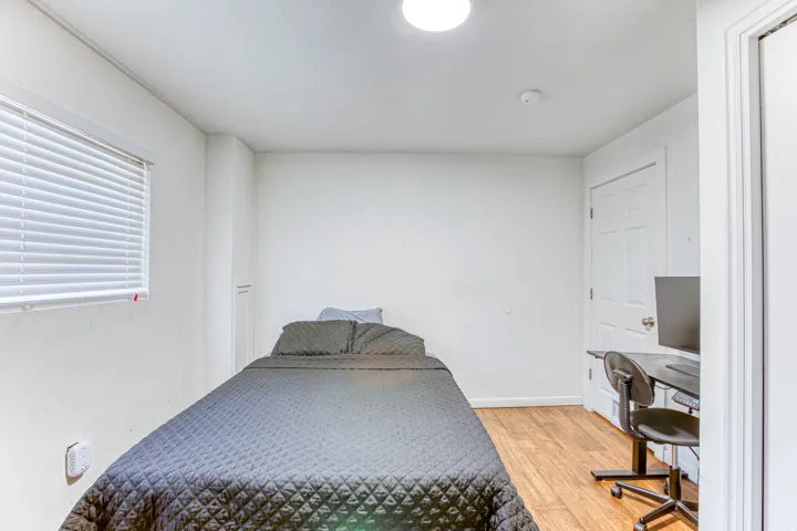 Room with wood-finish flooring, a white paneled door, and a single window with horizontal blinds