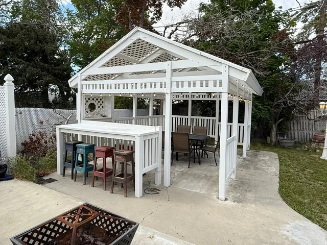 White wood gazebo featuring a lattice roof, integrated bar top, and built-in serving area, all set on a concrete patio
