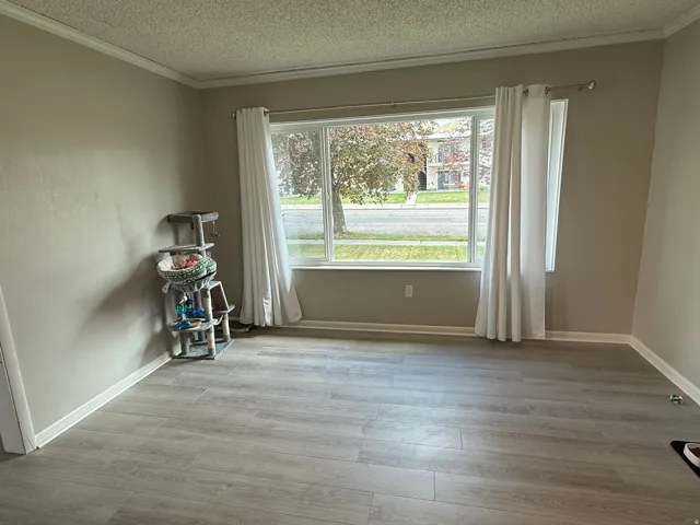 Spacious interior featuring wood-finish flooring, a large window, neutral wall tones, white trim, and crown molding