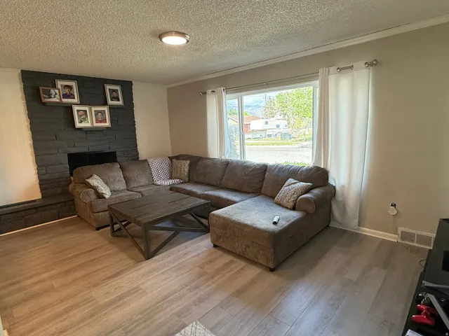 Living area featuring light wood-finish flooring, a dark stone-look fireplace surround, and a large window with white curtain panels