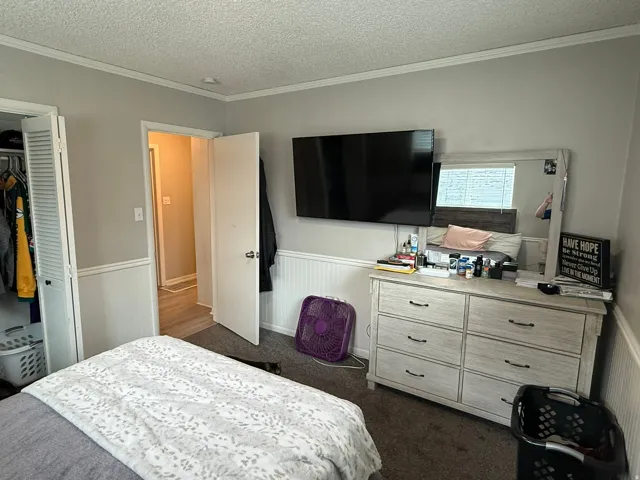 Bedroom featuring carpeting, wainscoting, crown molding, and a louvered bi-fold closet door