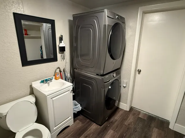 Compact utility space featuring wood-finish flooring, a white toilet, and a white vanity with a single basin sink