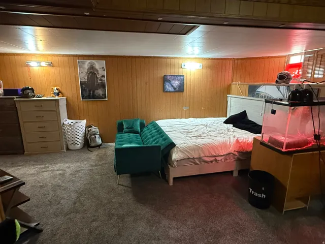 Carpeted room featuring wood-paneled walls and a built-in window with horizontal blinds
