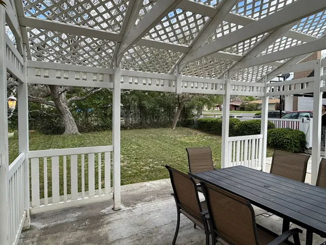 Patio featuring a white lattice pergola, concrete flooring, and a landscaped backyard with mature trees