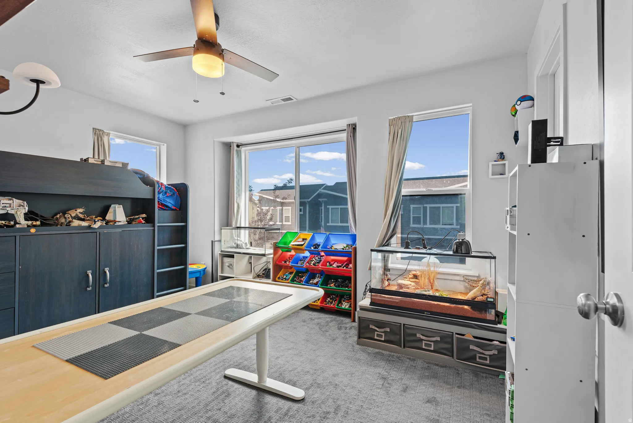 Carpeted room featuring a ceiling fan with integrated lighting, multiple windows, and a built-in bunk bed with integrated cabinetry
