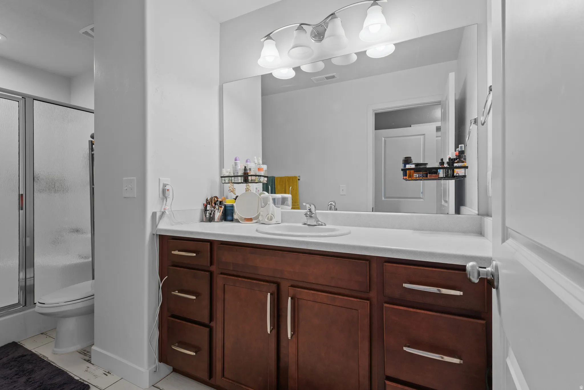 Bathroom vanity featuring a single basin sink, white countertop, and wood-finish cabinetry with silver-tone hardware