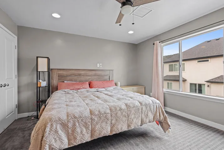 Spacious room with a wood-finish headboard, large window with natural light, recessed lighting, and a ceiling fan
