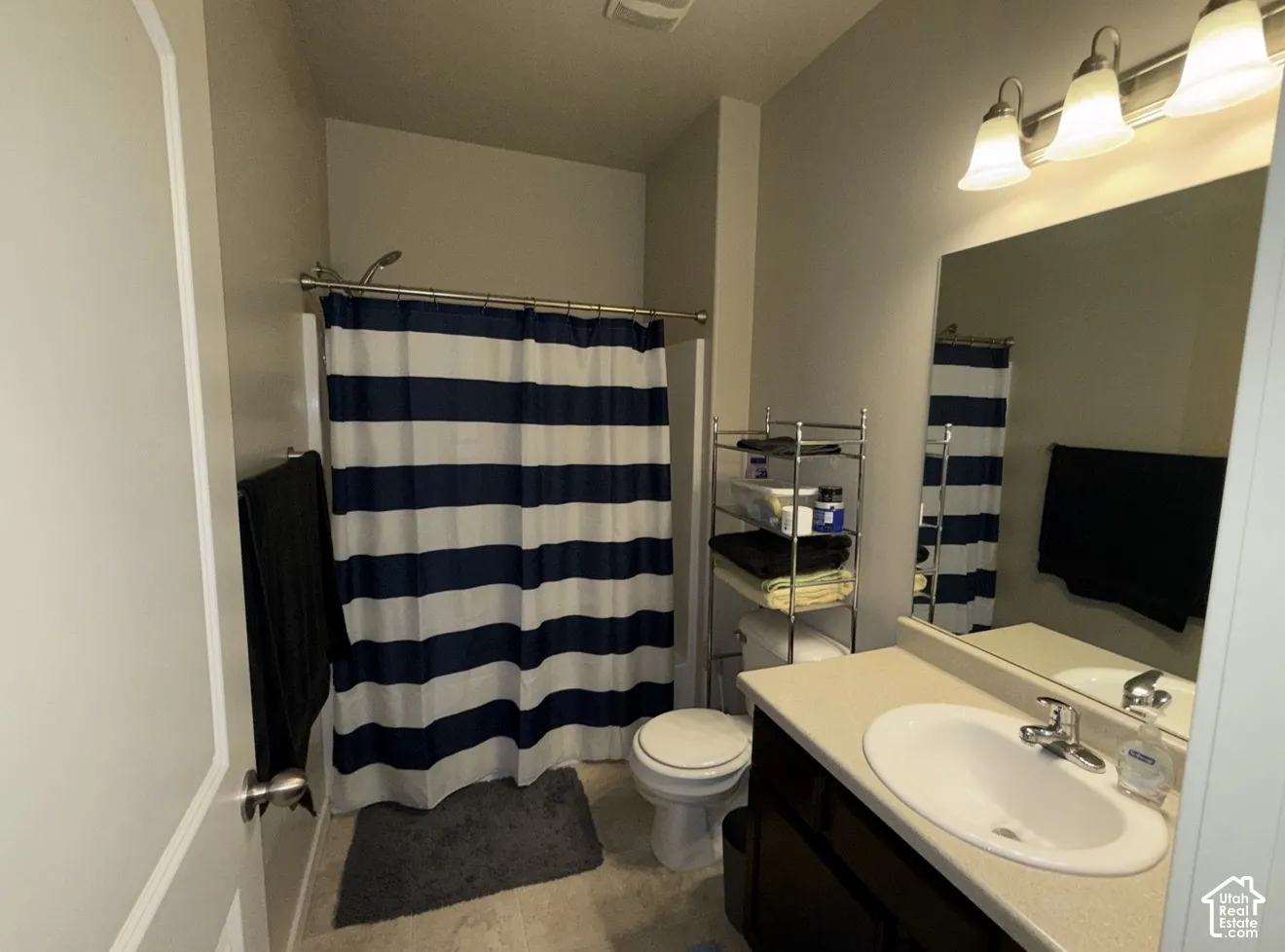 Full bathroom featuring a dark wood-finish vanity, solid surface countertop, integrated sink with chrome faucet, large wall-mounted mirror, and triple-light vanity fixture