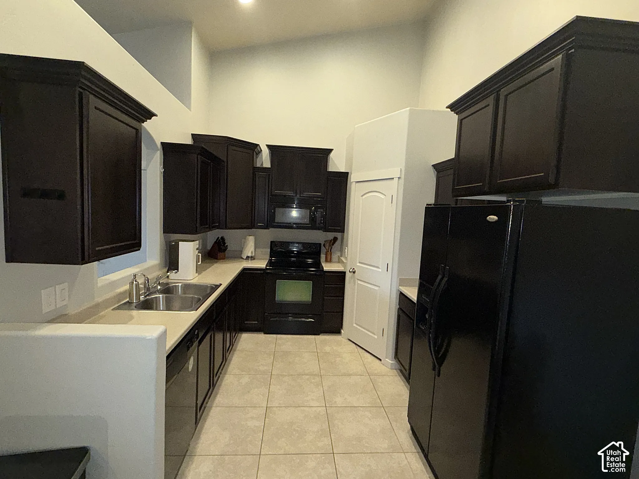 Kitchen featuring espresso-toned cabinetry, solid surface countertops, a dual-basin stainless steel sink, large-format tile flooring, and vaulted ceilings