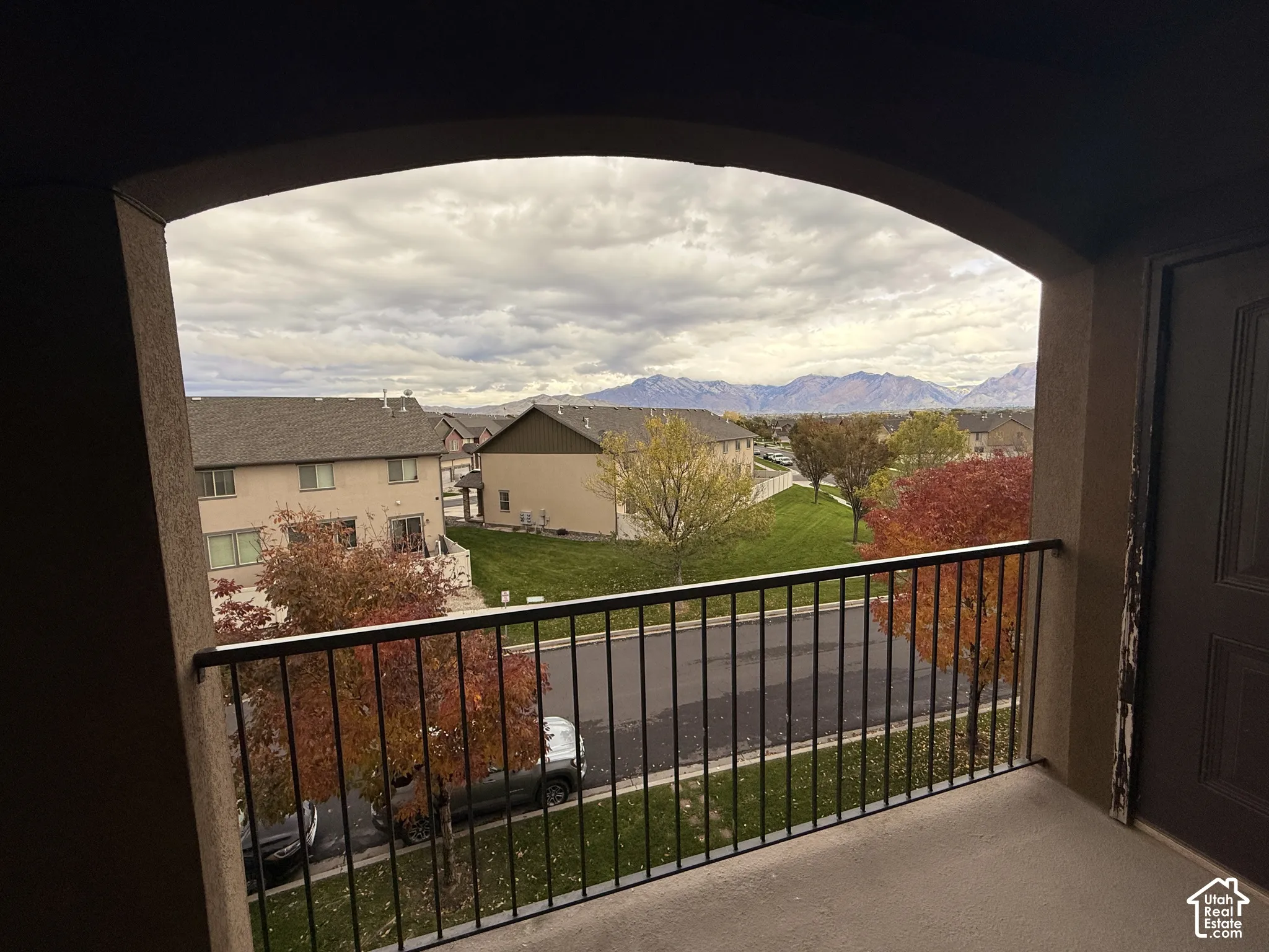 Covered balcony featuring an arched entryway and metal railing, overlooking mountain scenery and mature trees