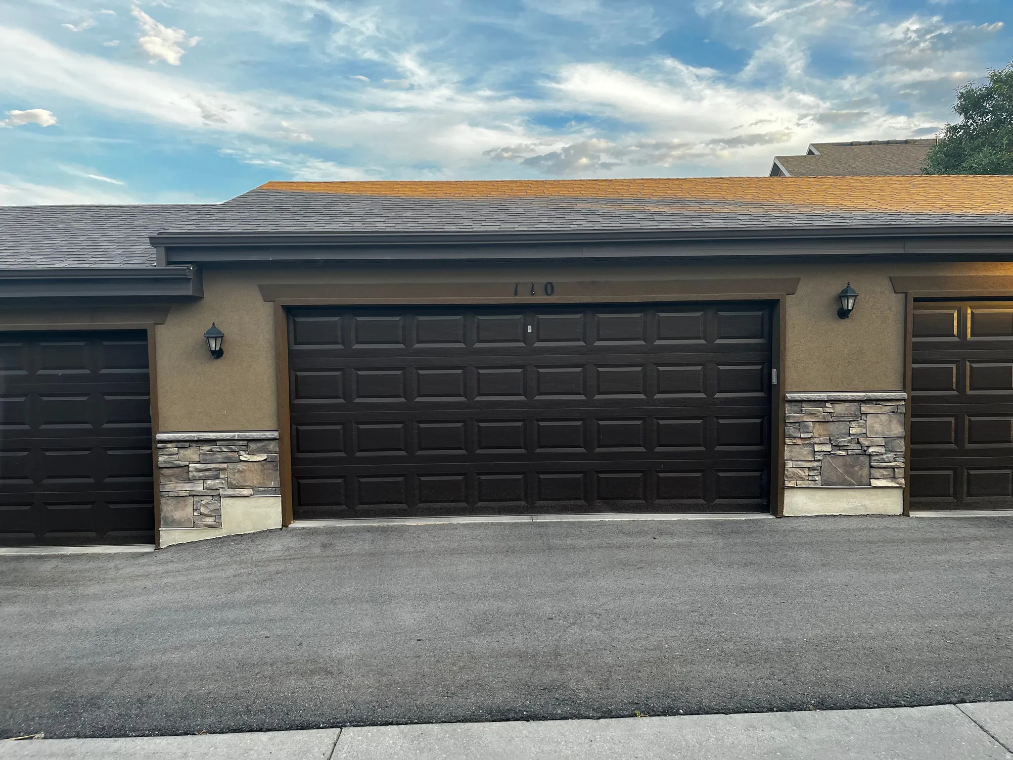 Multi-car garage featuring paneled doors, sconce lighting, and a stone facade accent