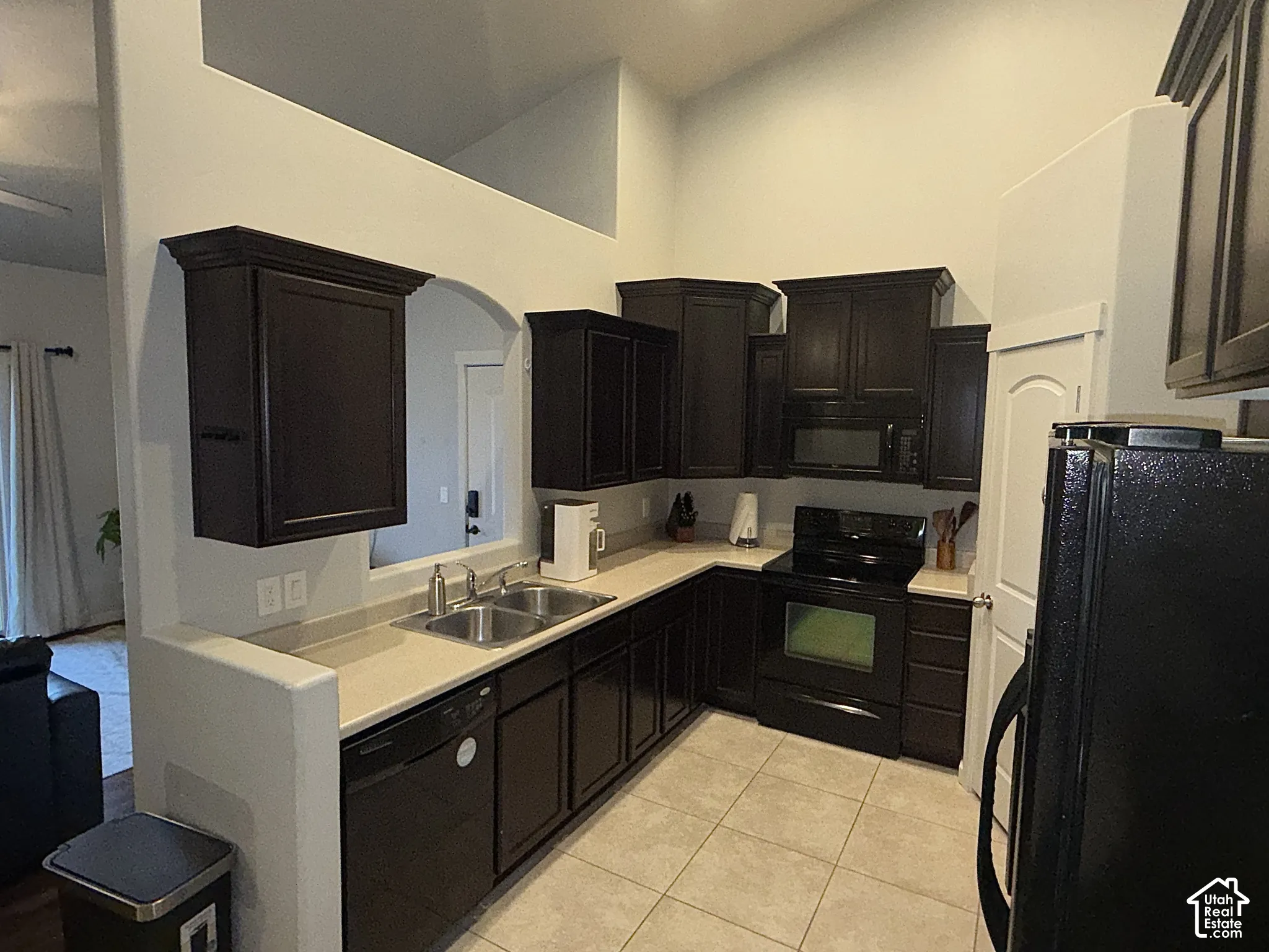 Kitchen featuring dark-finish cabinetry, neutral solid-surface countertops, tile flooring, vaulted ceilings, and a built-in microwave
