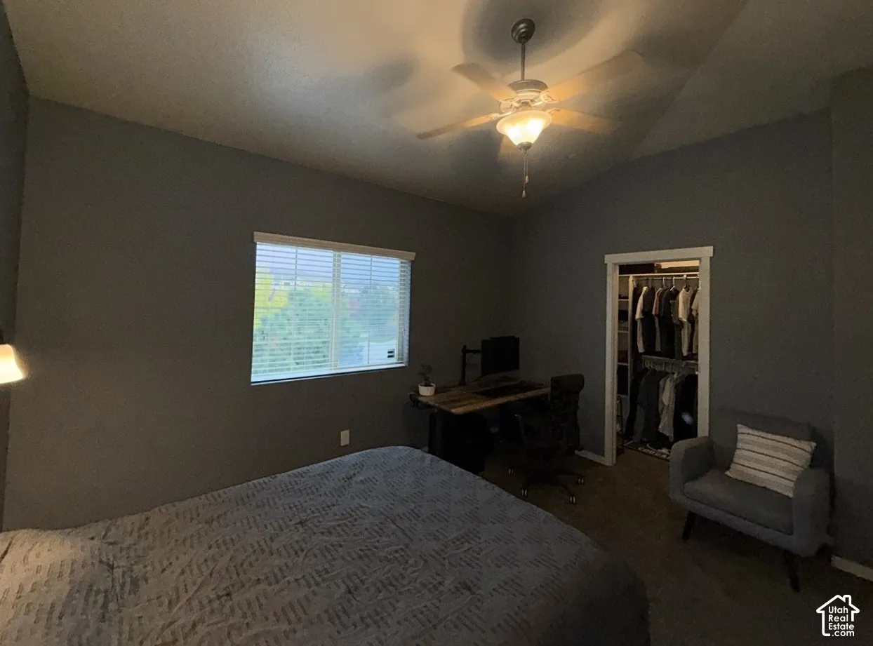 Vaulted ceilings, ceiling fan with integrated lighting, horizontal window blinds, and walk-in closet with built-in shelving