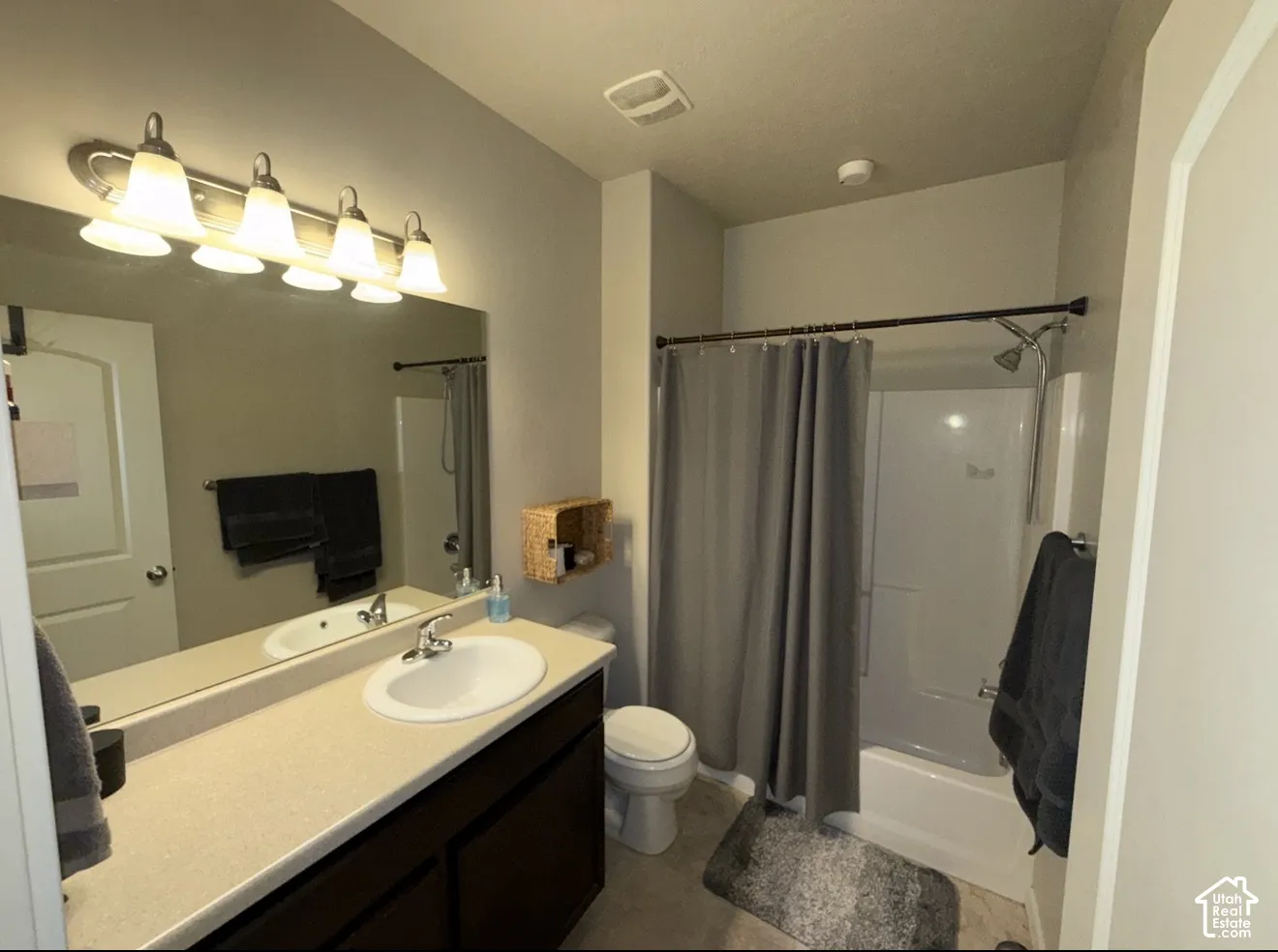 Bathroom featuring a large mirror, a wide vanity with a solid-surface countertop and integrated sink, a four-light fixture, and a tub-shower combination with a surround enclosure