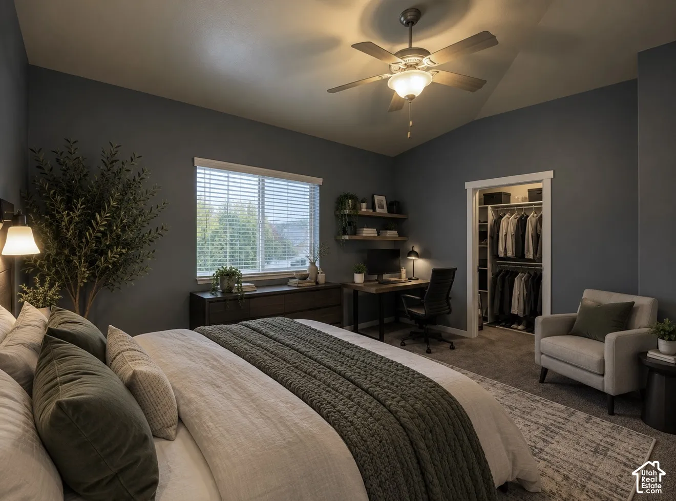 Vaulted ceiling featuring a central lighted ceiling fan, wall-mounted floating shelving, and a closet with built-in storage organizers