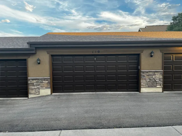 Multi-car garage featuring paneled doors, sconce lighting, and a stone facade accent