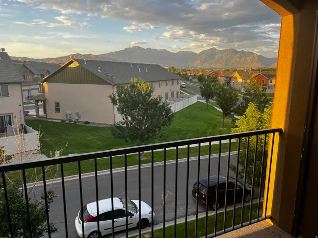 Balcony featuring a black wrought iron railing, overlooking a neighborhood with distant mountains