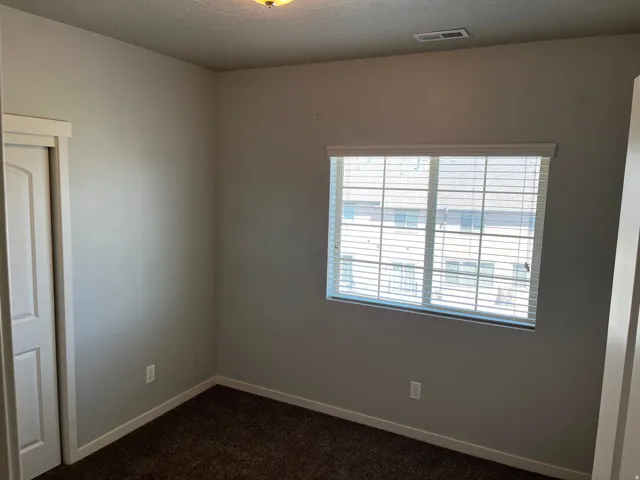 Room featuring a large window with horizontal blinds, neutral wall paint, dark carpet flooring, and white trim