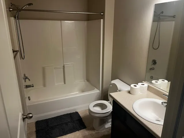 Full bathroom featuring a white tub/shower combination, polished chrome fixtures, a single vanity with a solid surface countertop, and an integrated sink