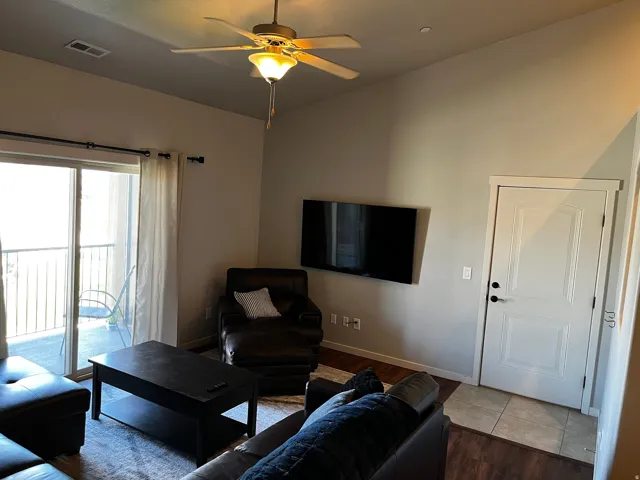 Living area featuring wood-finish flooring, a ceiling fan with integrated lighting, and a sliding glass door providing balcony access