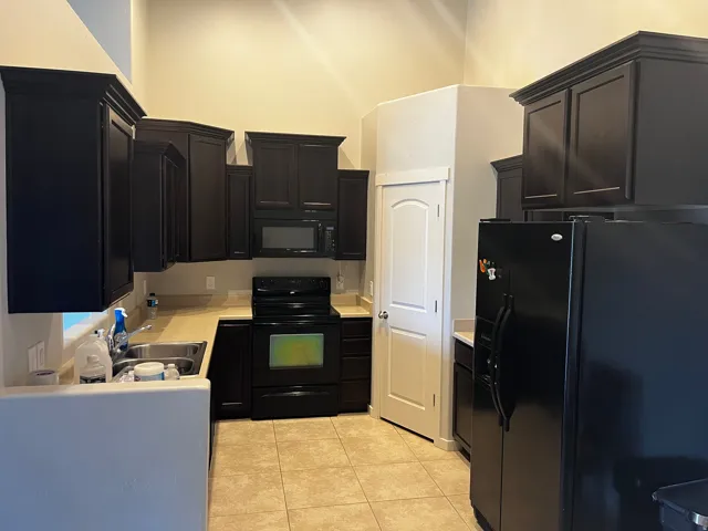 Kitchen featuring dark wood cabinetry, light beige countertops, and black appliances