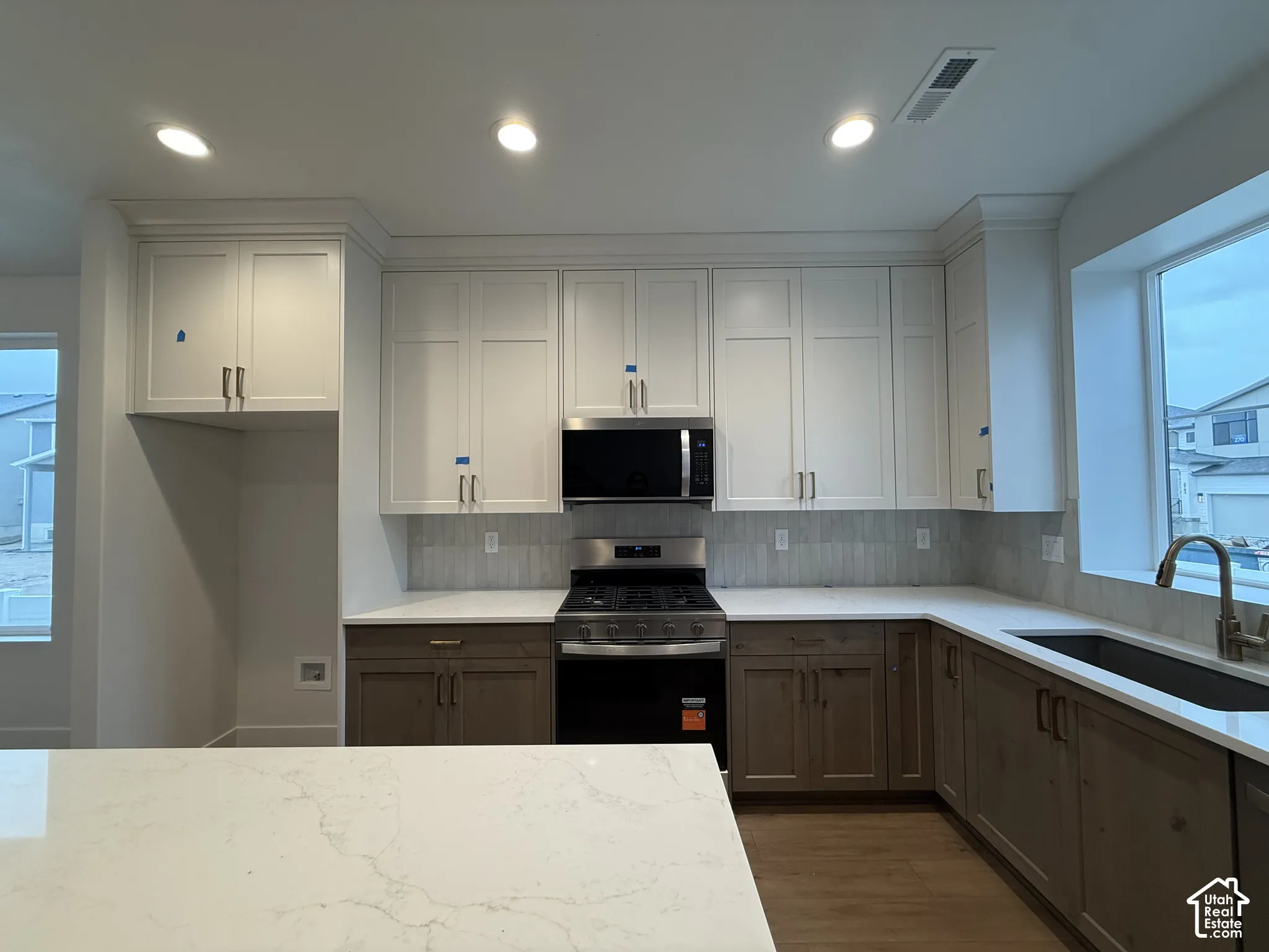 Kitchen featuring white upper cabinetry, two-tone lower cabinetry, light-toned countertops, tile backsplash, and a stainless steel gas range