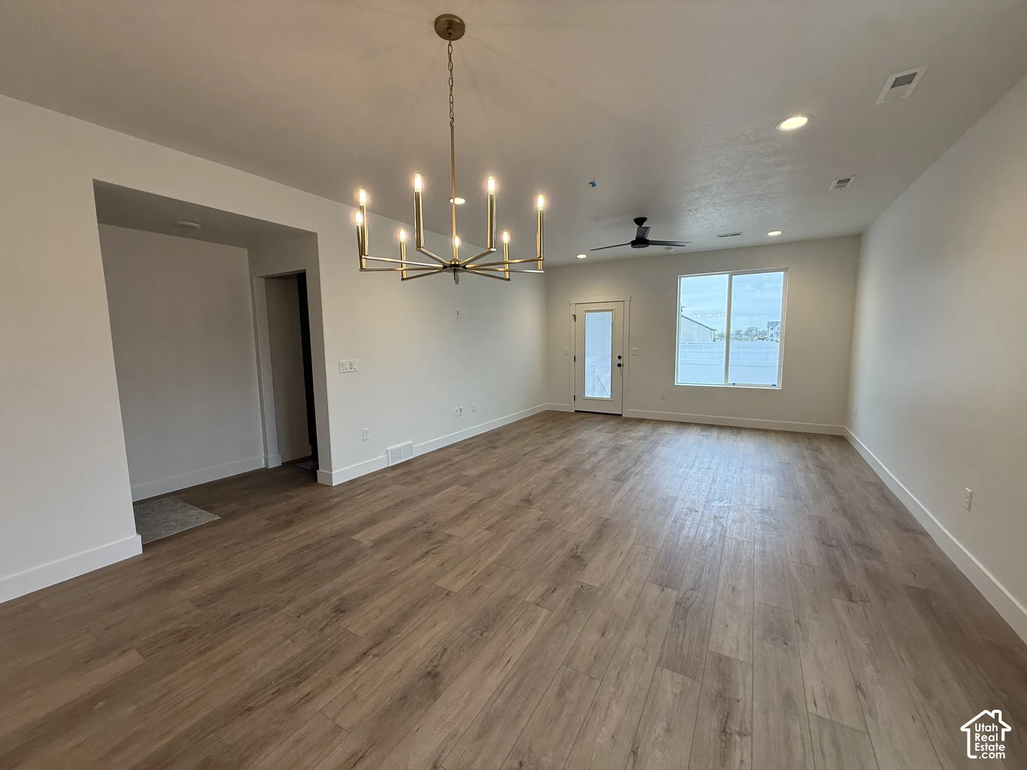 Spacious room featuring wood-finish flooring, a modern chandelier, recessed lighting, a ceiling fan, and access to an exterior door