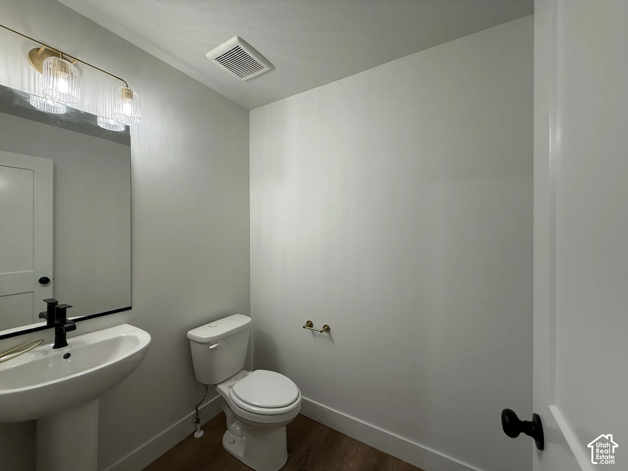 Pedestal sink with a black-finish faucet, rectangular mirror, and wood-finish flooring